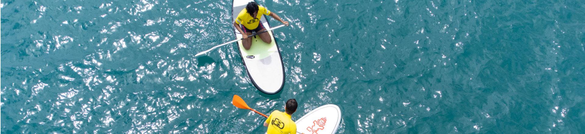 Two employees paddleboarding on clear blue water during a company retreat team-building activity and outdoor corporate getaway.