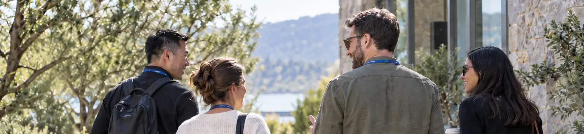 Four colleagues walk and talk together between sessions at an outdoor retreat venue, illustrating team building for new teams through informal conversation and relationship-building.